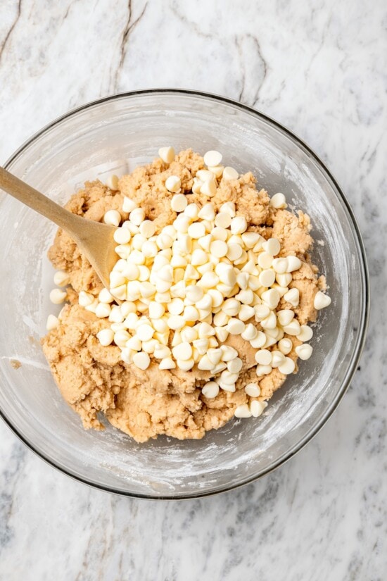 Overhead view of white chocolate chips being folded into bowl of dough
