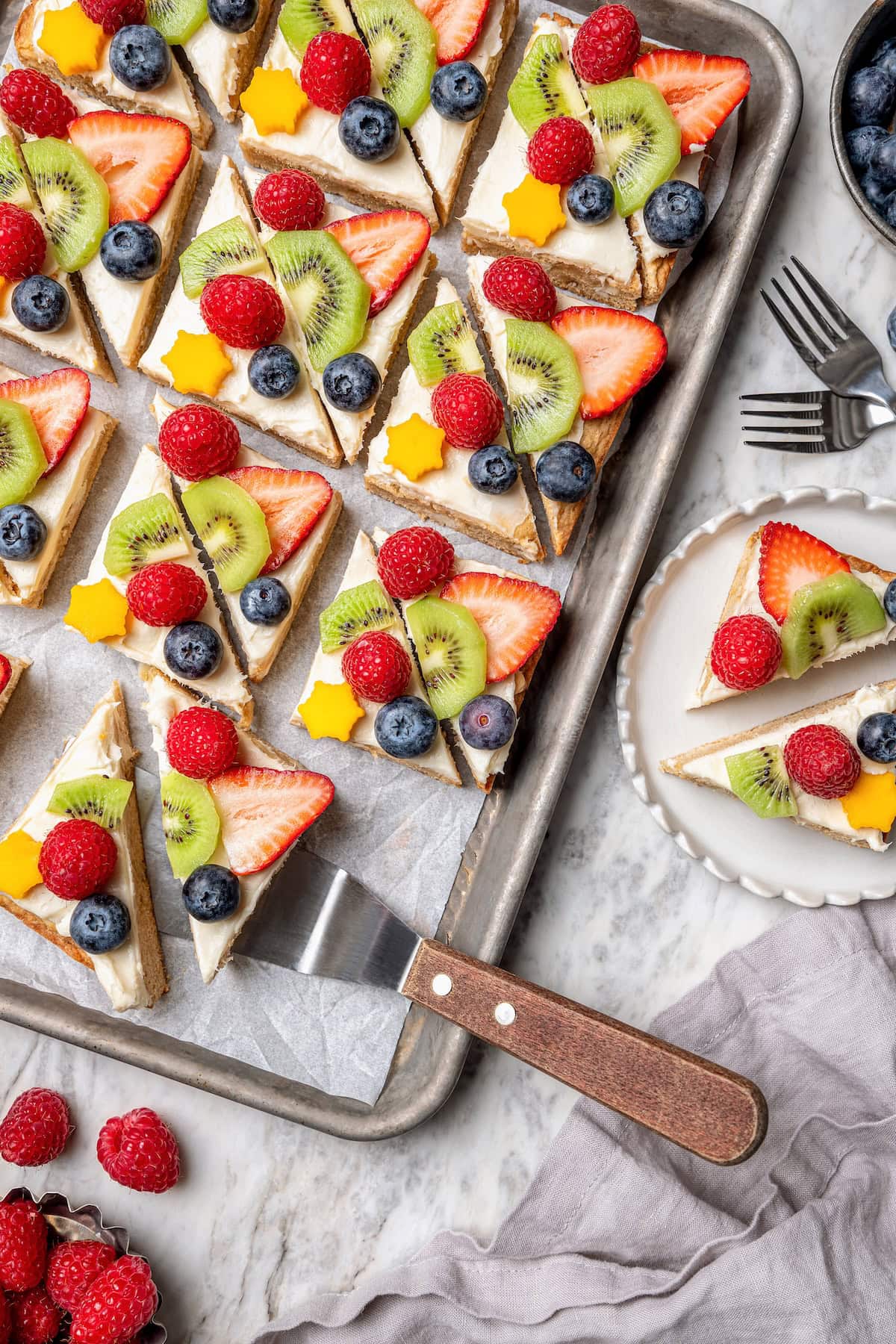 Overhead view of fruit pizza on sheet pan and plate