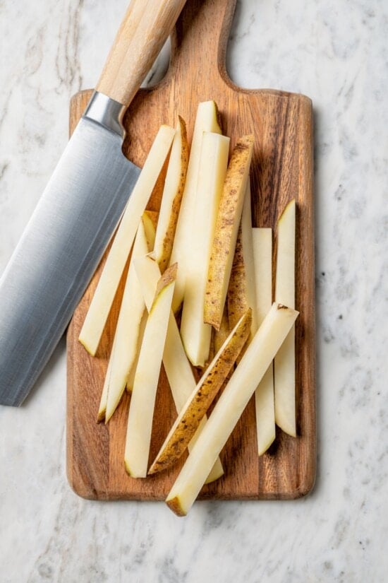 This lightened up Peruvian lomo saltado recipe is packed with flavor, with tender sirloin and veggies served alongside crispy baked fries. Overhead view of potato cut into fries on cutting board