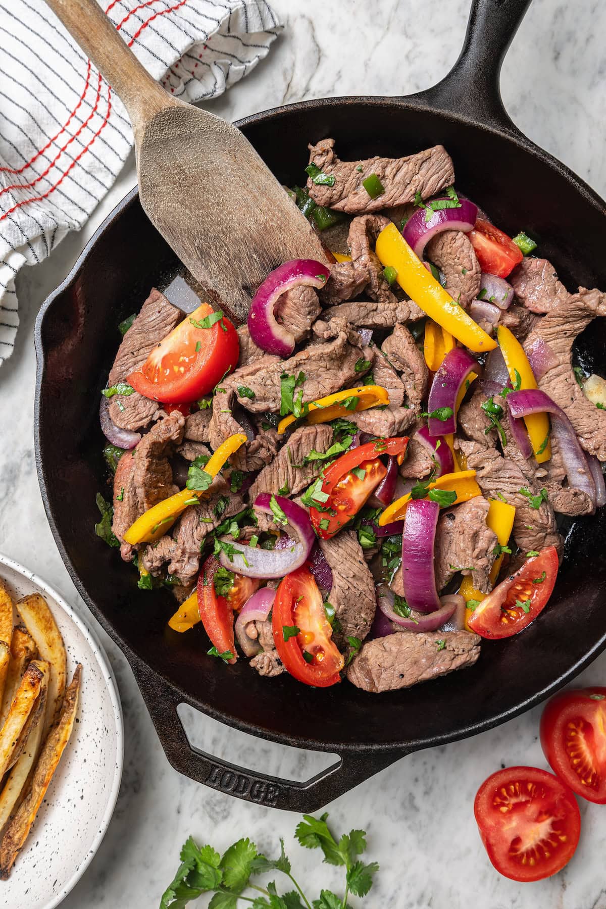 This lightened up Peruvian lomo saltado recipe is packed with flavor, with tender sirloin and veggies served alongside crispy baked fries. Overhead view of lomo saltado cooking in skillet