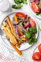 Peruvian lomo saltado on plate with fork and sprig of cilantro
