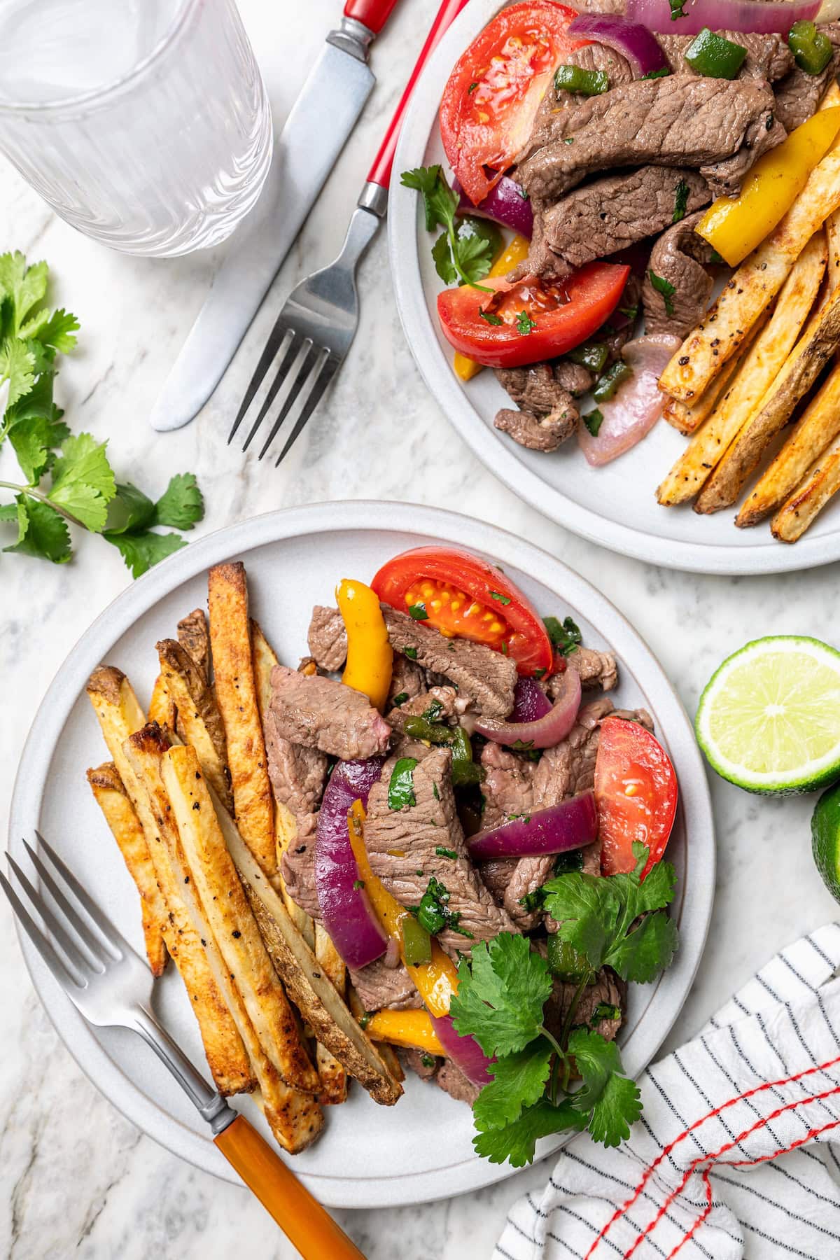 This lightened up Peruvian lomo saltado recipe is packed with flavor, with tender sirloin and veggies served alongside crispy baked fries. Two plates with Peruvian lomo saltado