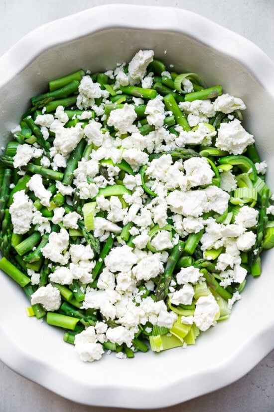 Add veggies and feta to a quiche dish.