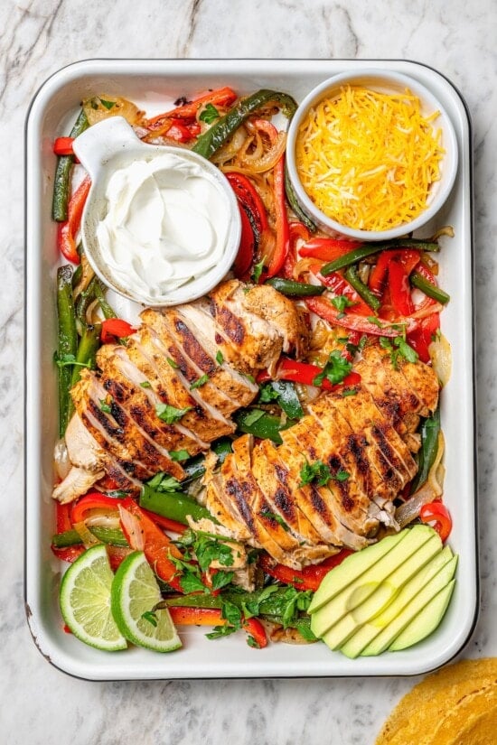 Overhead view of chicken fajitas in pan with avocado, cheese, and sour cream