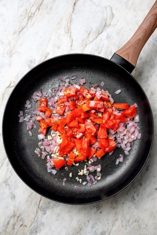 Tomatoes added to skillet of red onions