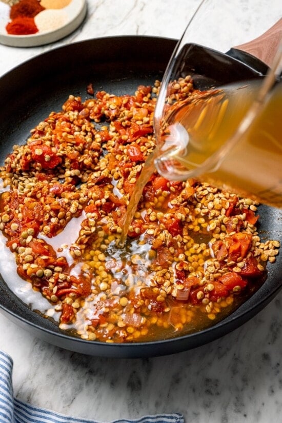 Pouring broth into pan with lentils and tomatoes