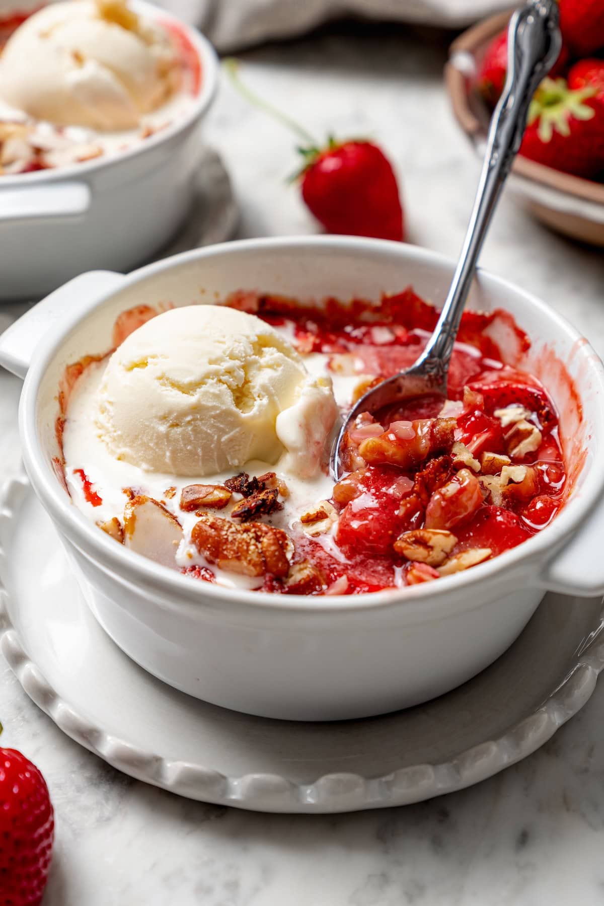 Spoon digging into healthy strawberry crisp topped with ice cream
