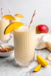 Mango lassi in glass with straw and mango slice on rim for garnish