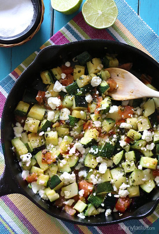 Mexican zucchini in a black cast iron skillet with a wooden spoon.