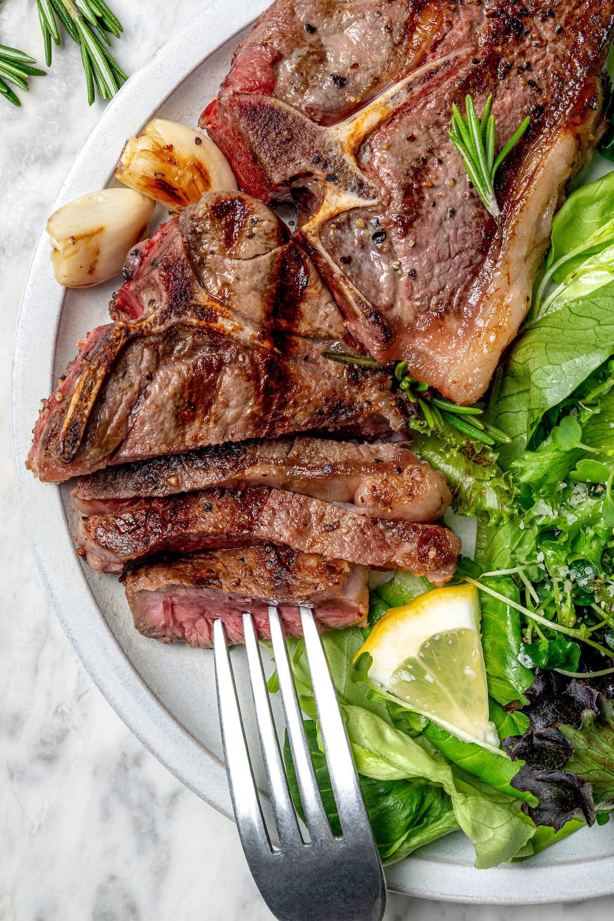 Sliced grilled lamb chop on plate with salad and fork