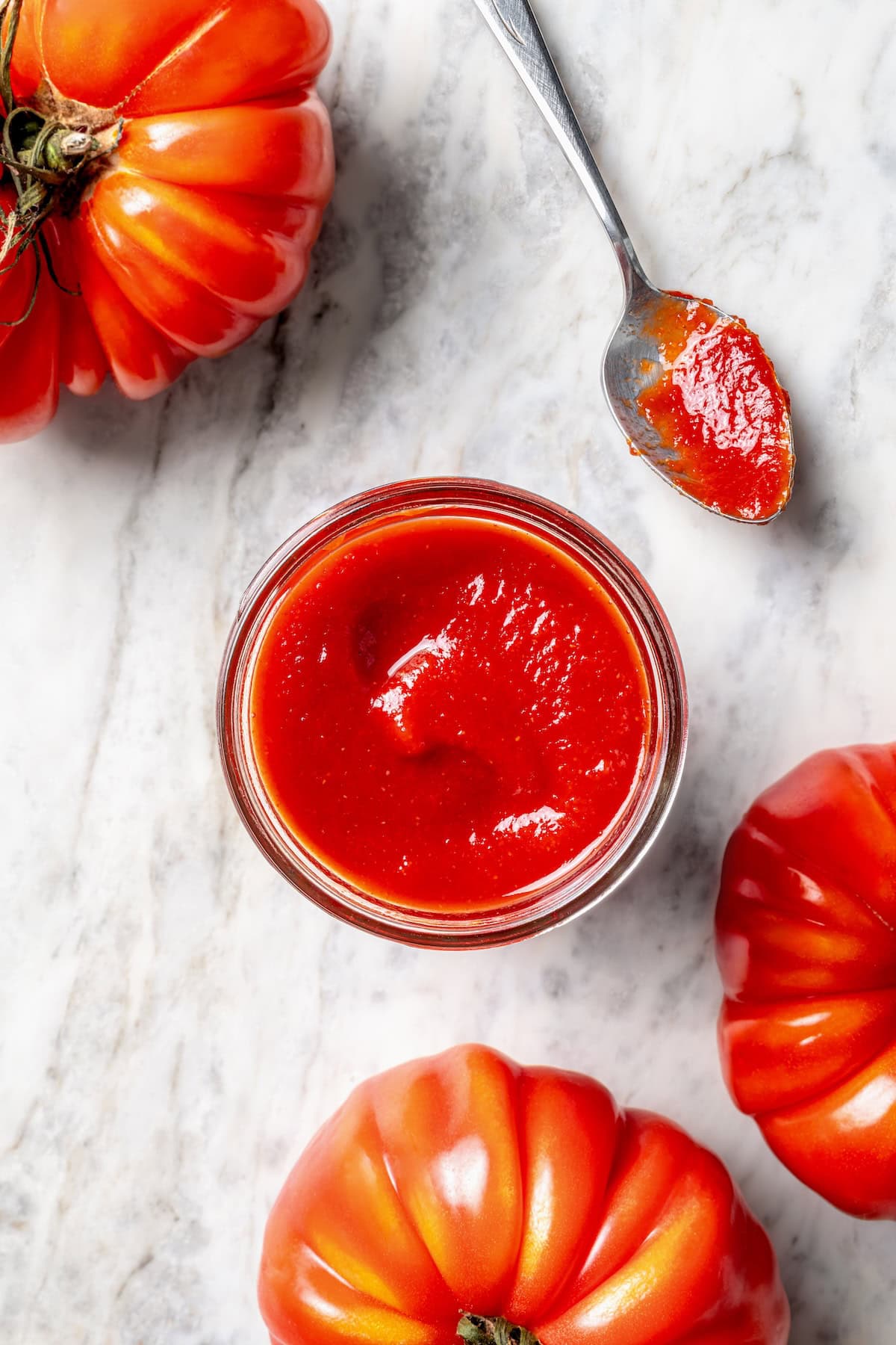 Overhead view of homemade ketchup in jar and spoon, surrounded by fresh heirloom tomatoes
