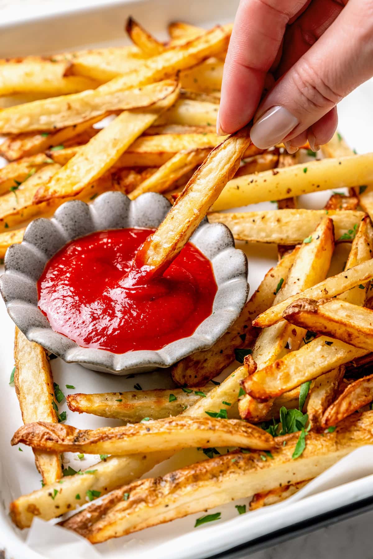 Hand dipping fry into bowl of homemade ketchup