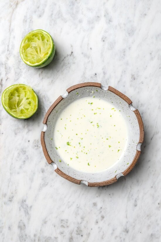 Overhead view of lime mayo in bowl set next to 2 juiced lime halves