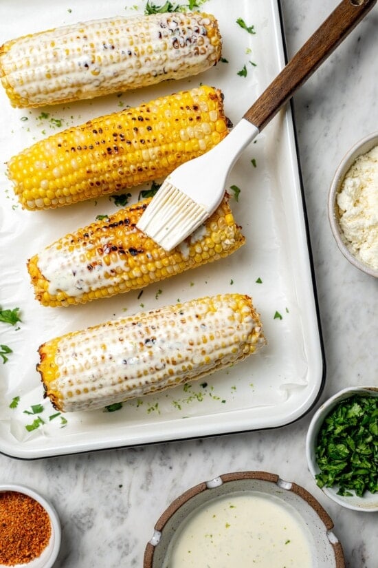 Brushing grilled corn with lime mayo mixture