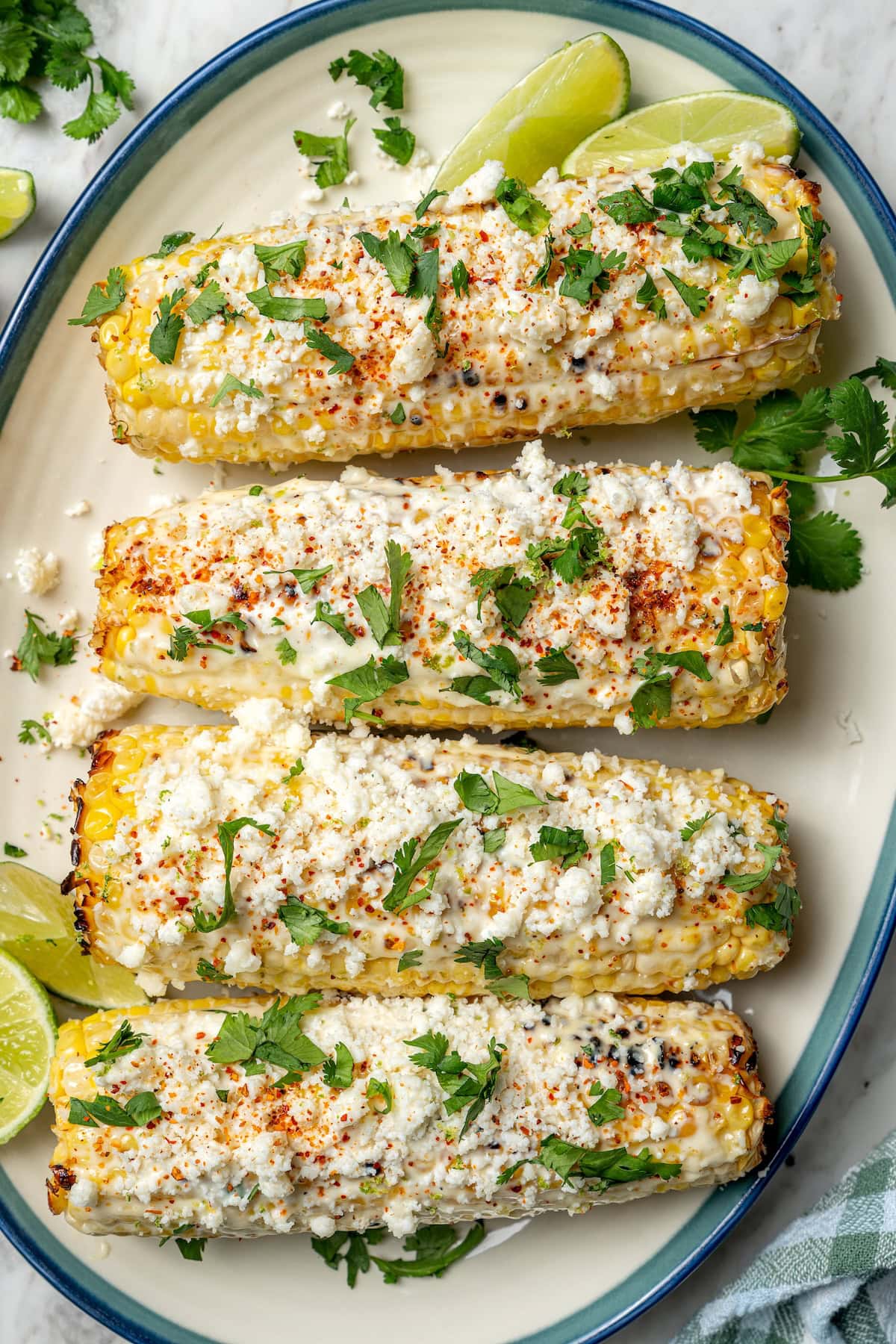 Overhead view of 4 ears of Mexican street corn on platter with cilantro and lime wedges