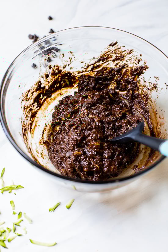 Zucchini brownie batter in glass mixing bowl with rubber spatula
