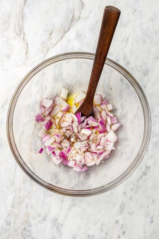 With juicy, ripe tomatoes, red onion, briny olives and fresh basil, this easy heirloom tomato salad recipe is absolutely packed with flavor! Overhead view of onions in bowl with olive oil, salt, and pepper