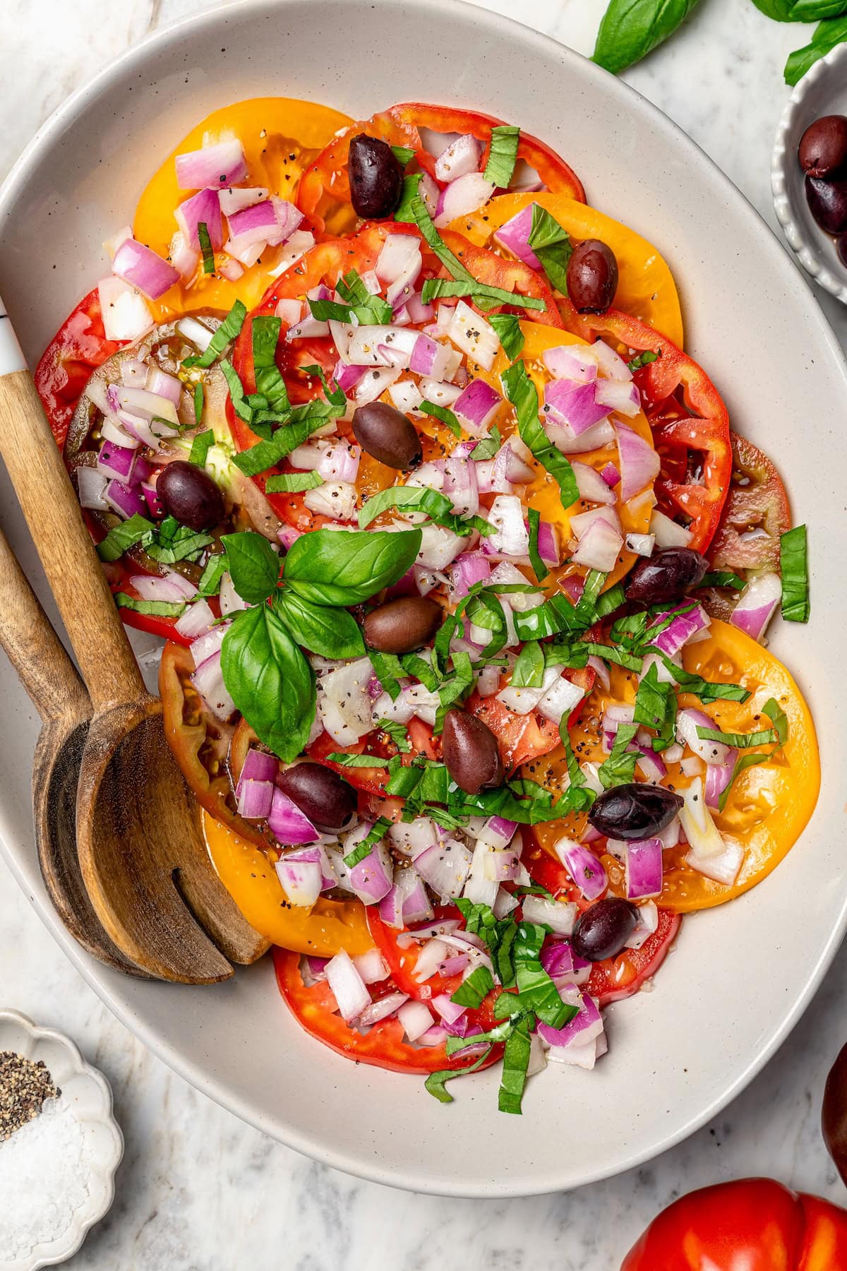 With juicy, ripe tomatoes, red onion, briny olives and fresh basil, this easy heirloom tomato salad recipe is absolutely packed with flavor! Overhead view of heirloom tomato salad on platter with serving spoons