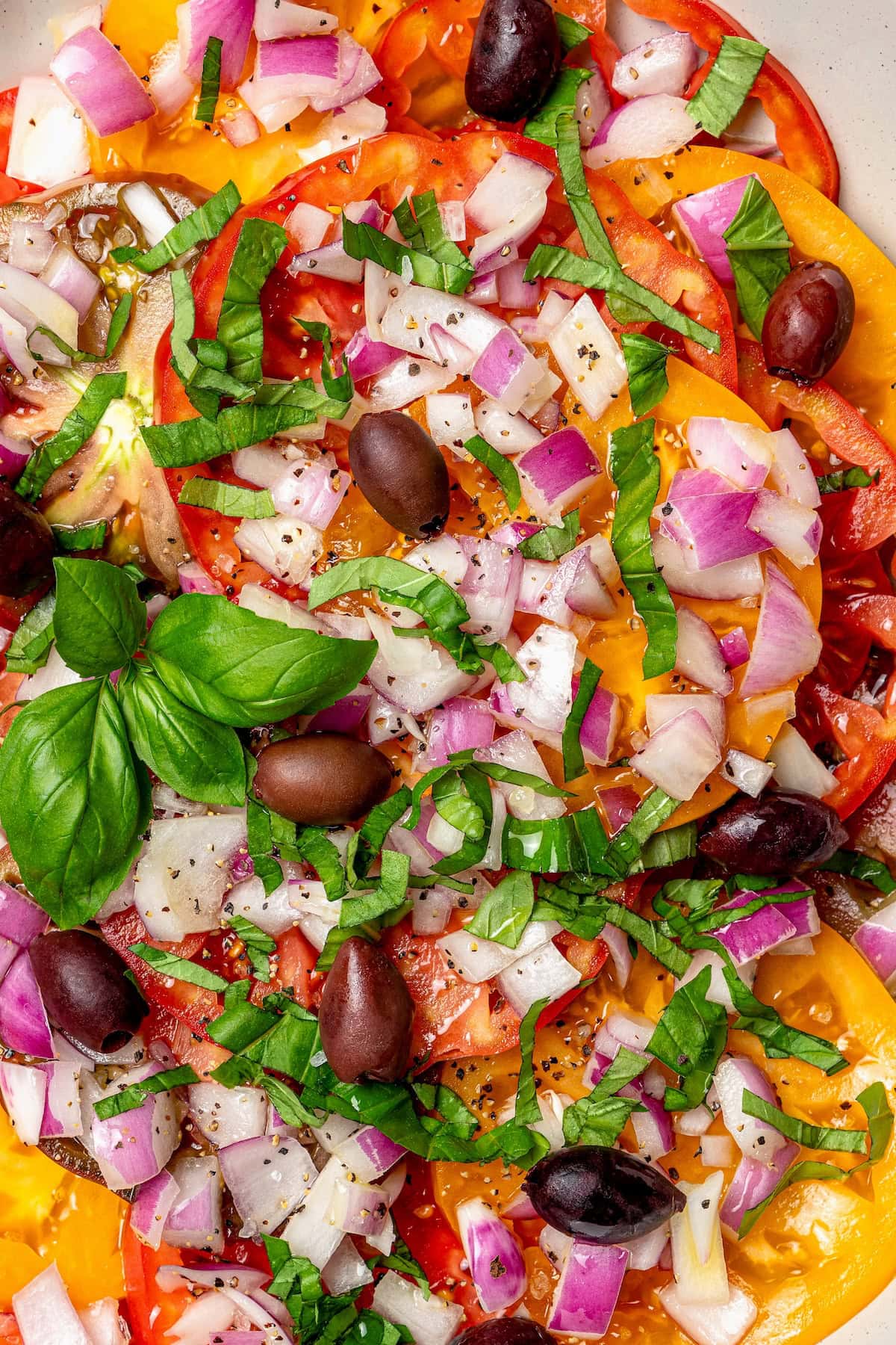 With juicy, ripe tomatoes, red onion, briny olives and fresh basil, this easy heirloom tomato salad recipe is absolutely packed with flavor! Overhead view of heirloom tomato salad with kalamata olives, basil, and red onion