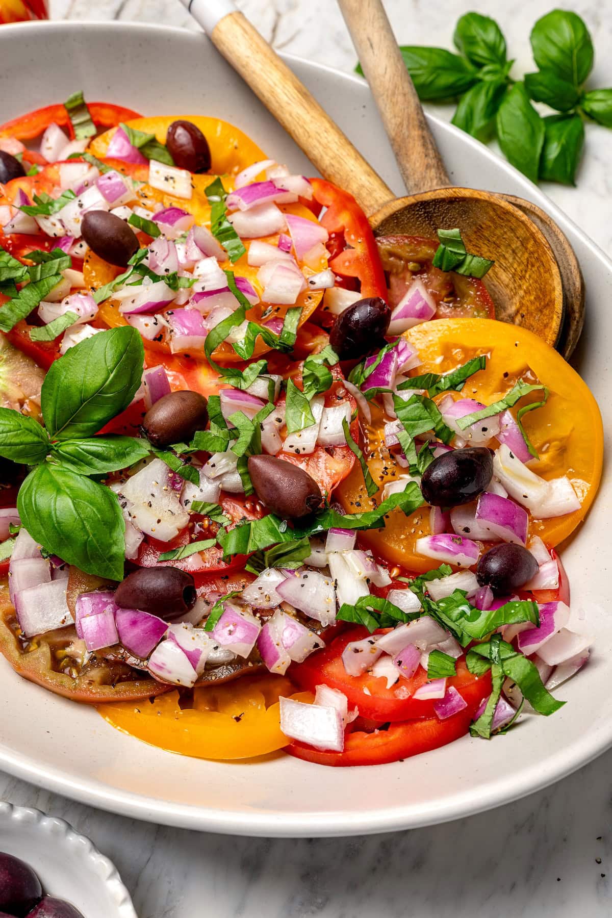 With juicy, ripe tomatoes, red onion, briny olives and fresh basil, this easy heirloom tomato salad recipe is absolutely packed with flavor! Heirloom tomato salad on platter with olives and onions