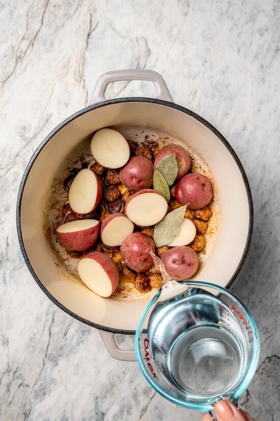 Pouring water into Dutch oven with bay leaves and potatoes