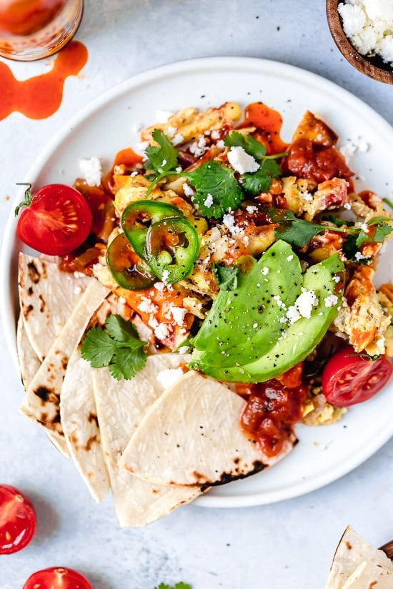 Overhead view of migas on plate with tortillas and avocado