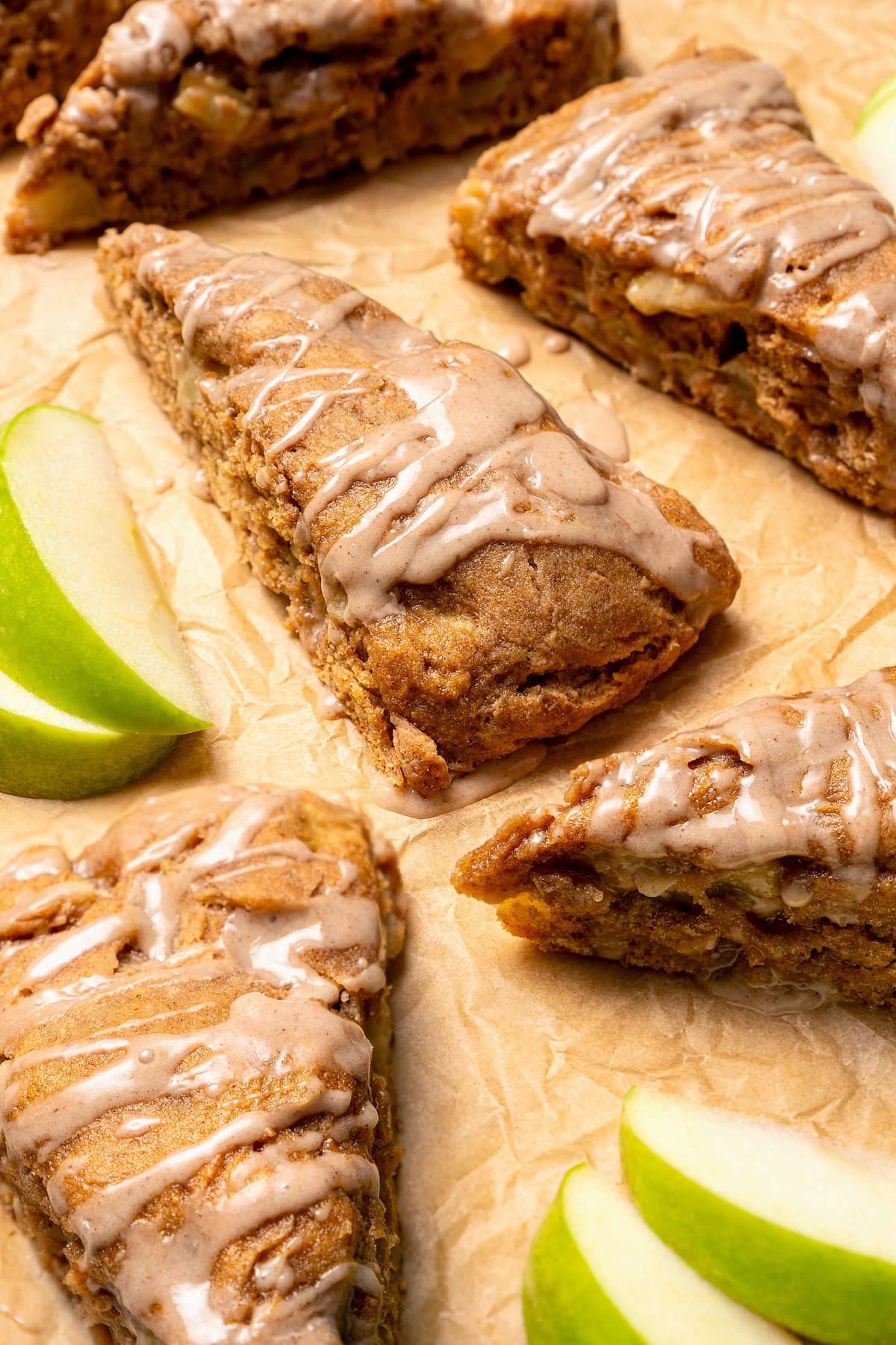 Buttermilk gives these spiced apple scones a moist, tender crumb, while applesauce replaces much of the butter to lighten them up! Glazed apple scones set on parchment paper