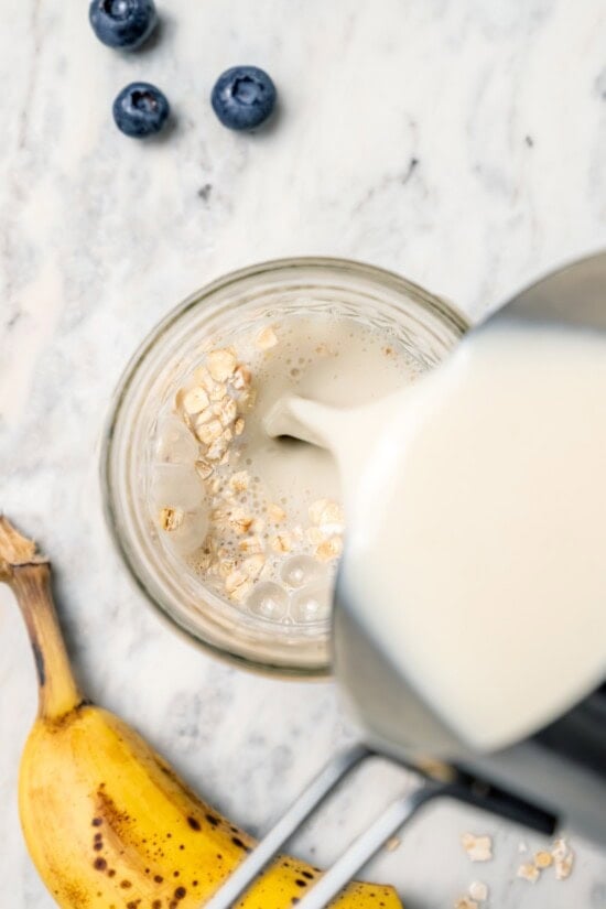 Overhead view of milk being poured into jar of overnight oats
