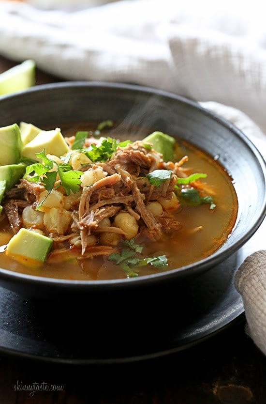 Bowl of pozole rojo with avocado and cilantro for garnish.