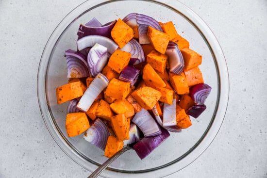 Potatoes, red onion in a bowl with seasoning.
