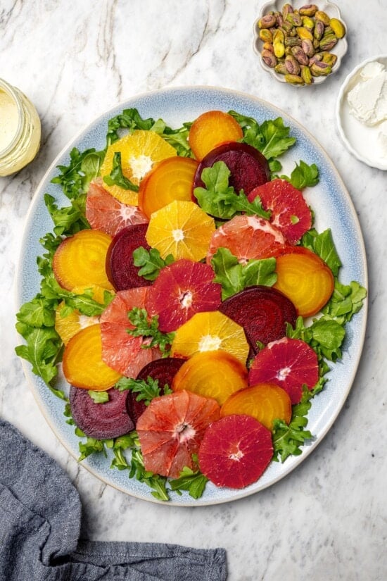 This Roasted Beet and Citrus Salad pairs tender beets with creamy goat cheese, citrus fruit and pistachios for a show-stopping holiday side! Sliced beets and citrus fruit on platter with arugula.