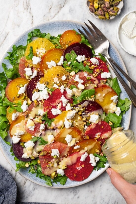 This Roasted Beet and Citrus Salad pairs tender beets with creamy goat cheese, citrus fruit and pistachios for a show-stopping holiday side! Pouring vinaigrette onto roasted beet and citrus salad.
