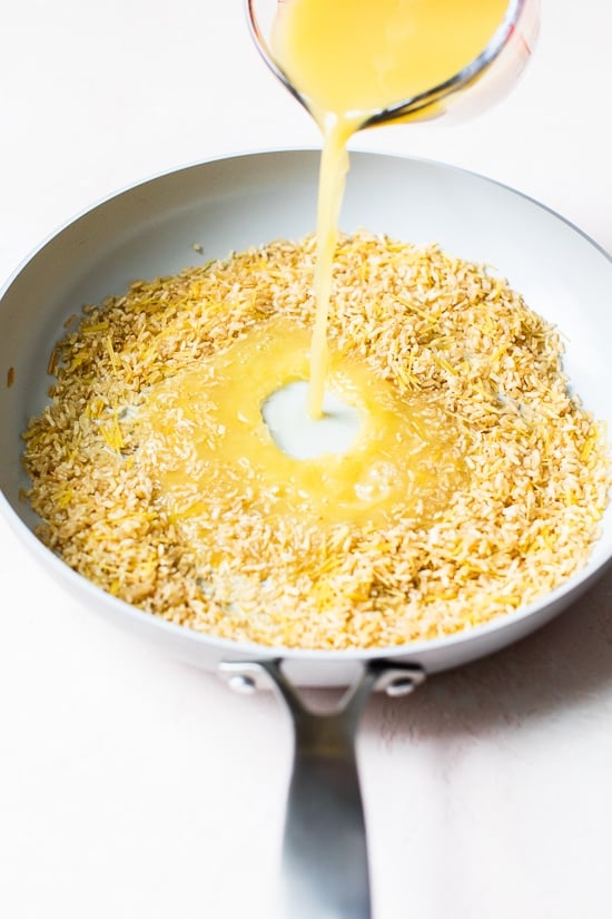 Pouring broth into skillet of rice and pasta for pilaf.