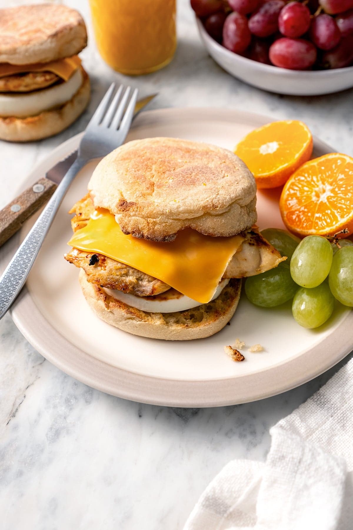 Copycat Chick-fil-A egg white grill sandwich on plate with grapes and orange halves.