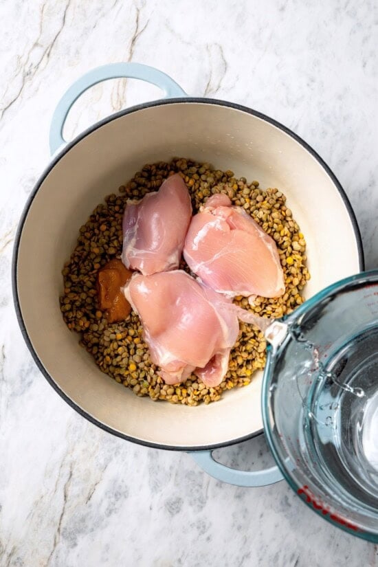 Pouring water into pot with lentils and raw chicken.