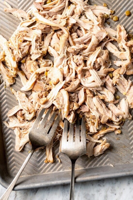 Two forks shredding chicken on sheet pan.