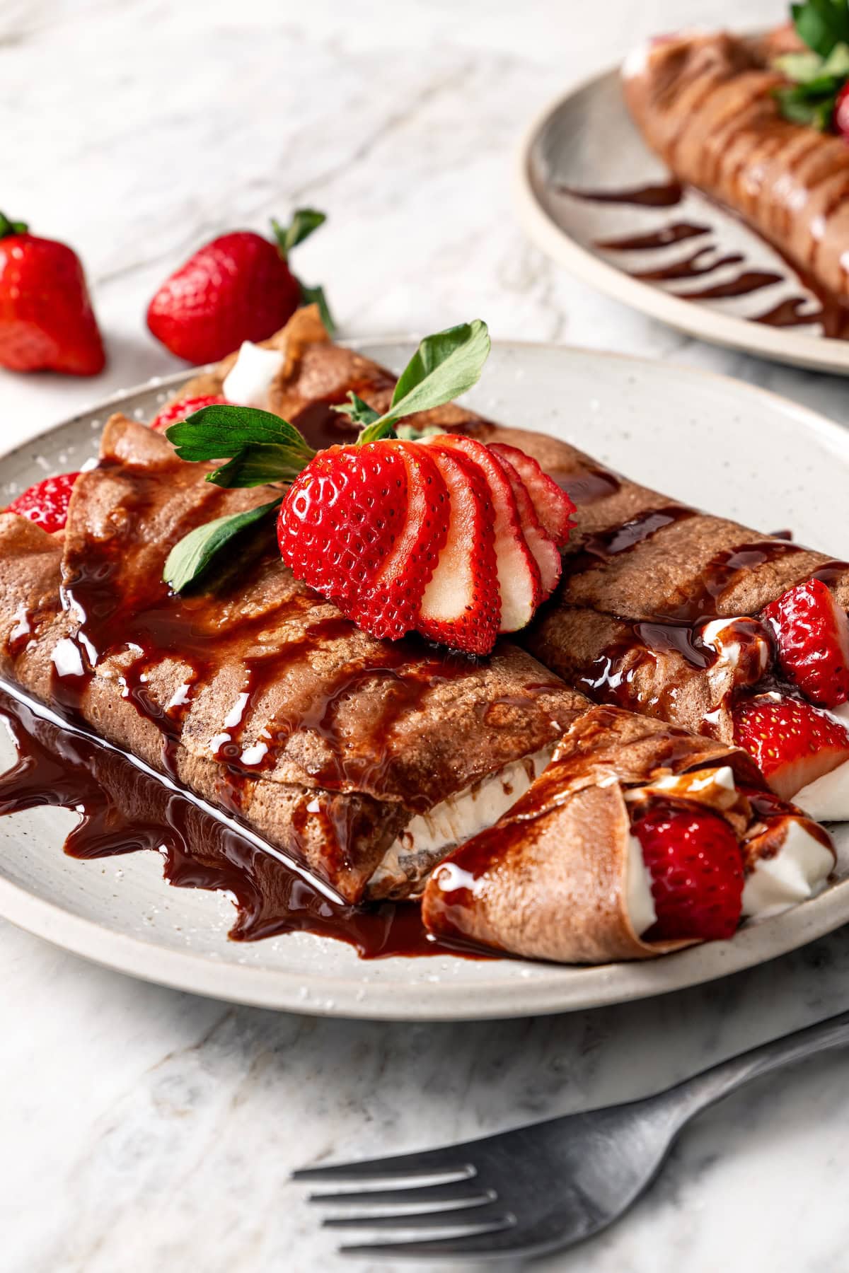 Two chocolate crepes filled with whipped cream and strawberries.