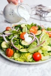 Pouring buttermilk ranch dressing onto garden salad.