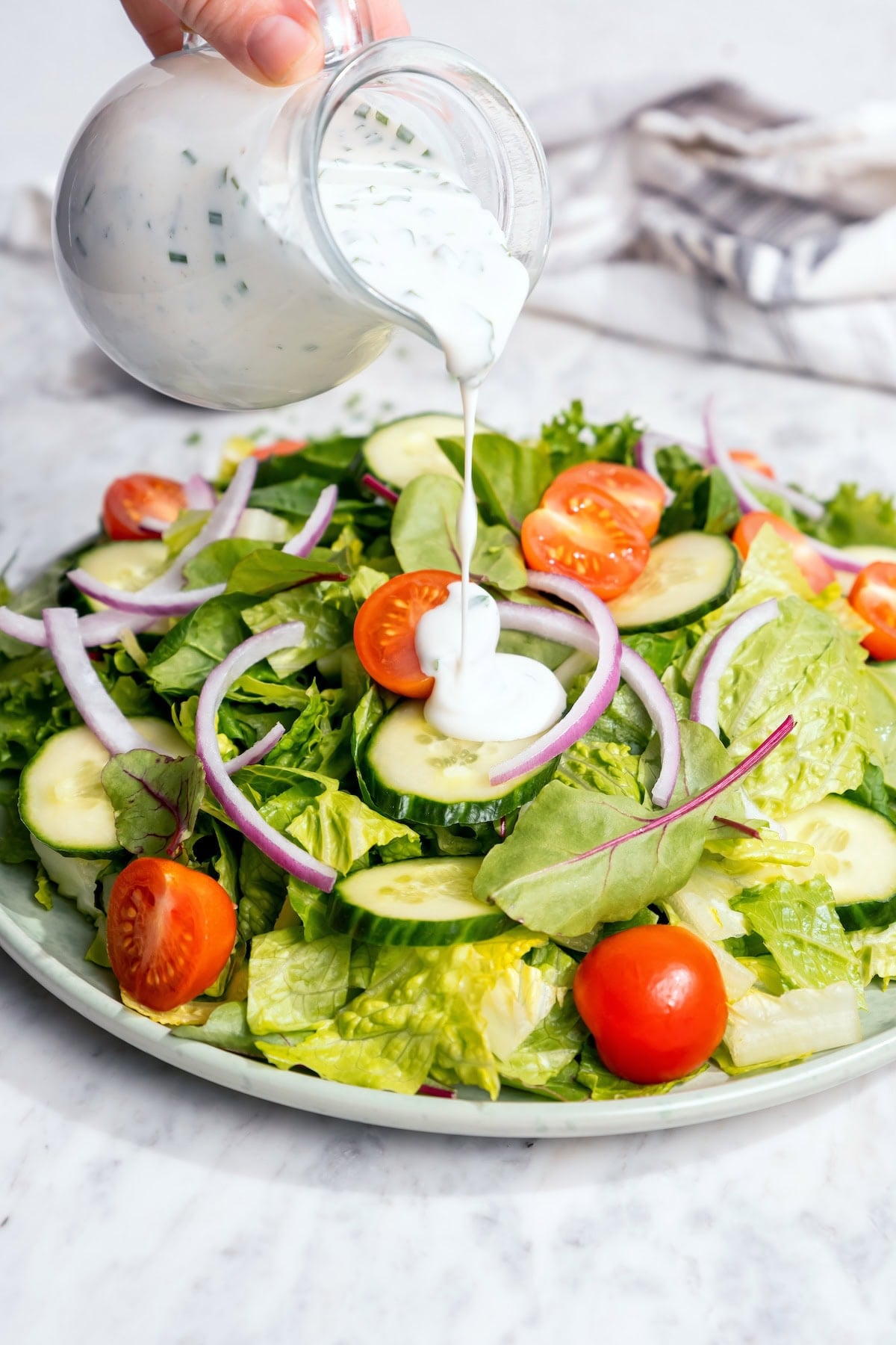 Pouring buttermilk ranch dressing onto garden salad.