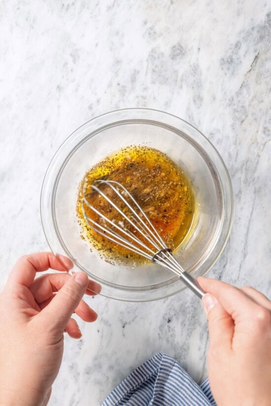 Whisking Greek salad dressing in small glass bowl.