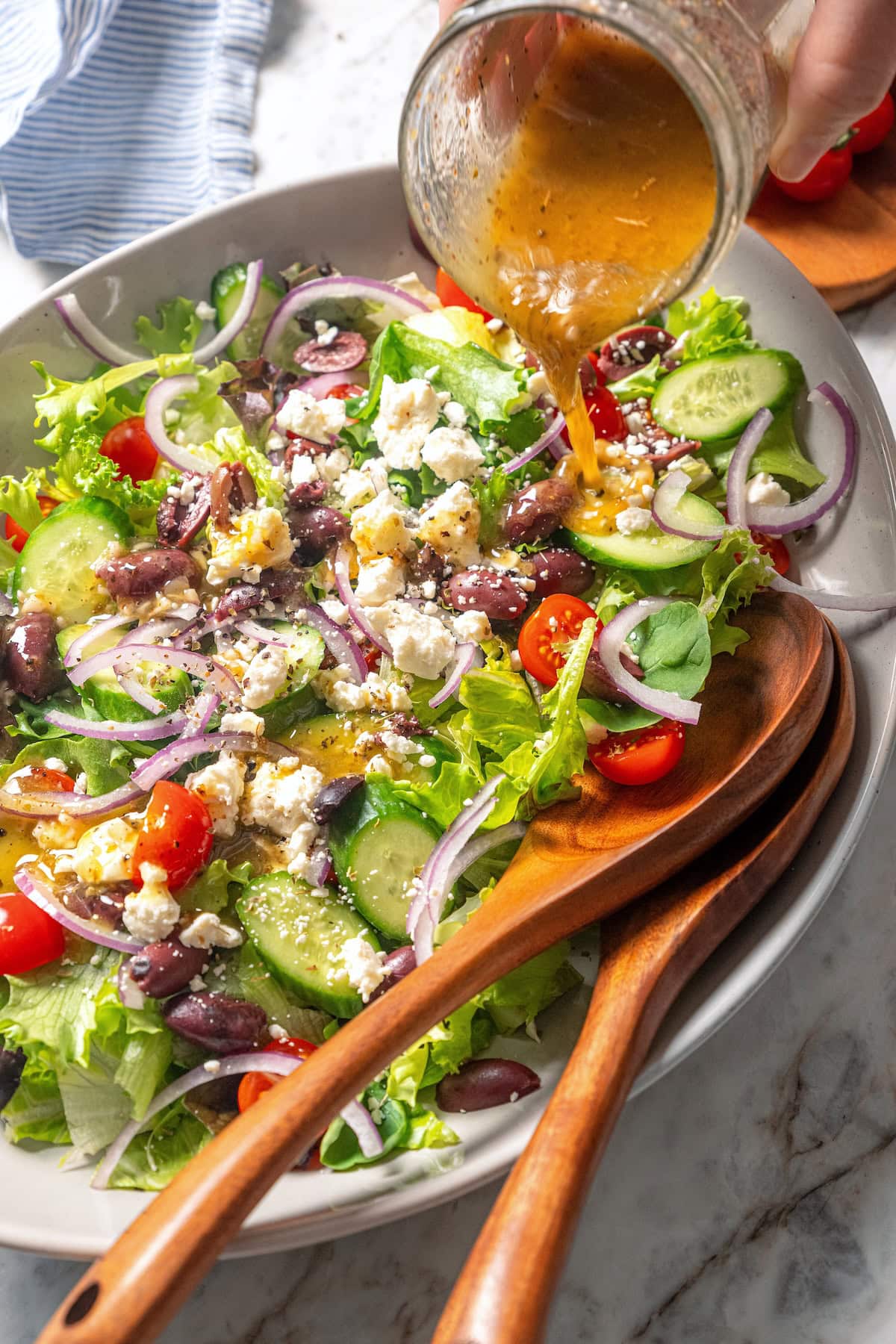 Pouring Greek salad dressing over bowl of salad.