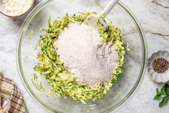 Whole wheat flour added to bowl of shredded zucchini.