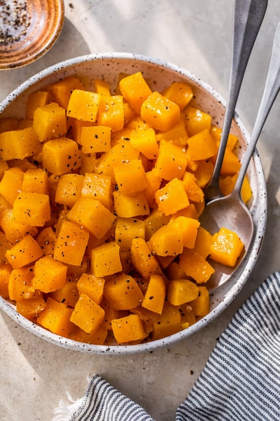 This easy maple roasted butternut squash is a quick fall side dish with cubed squash tossed in pure maple syrup. Perfect for holiday dinners! Diced maple roasted butternut squash with black pepper in a white bowl.