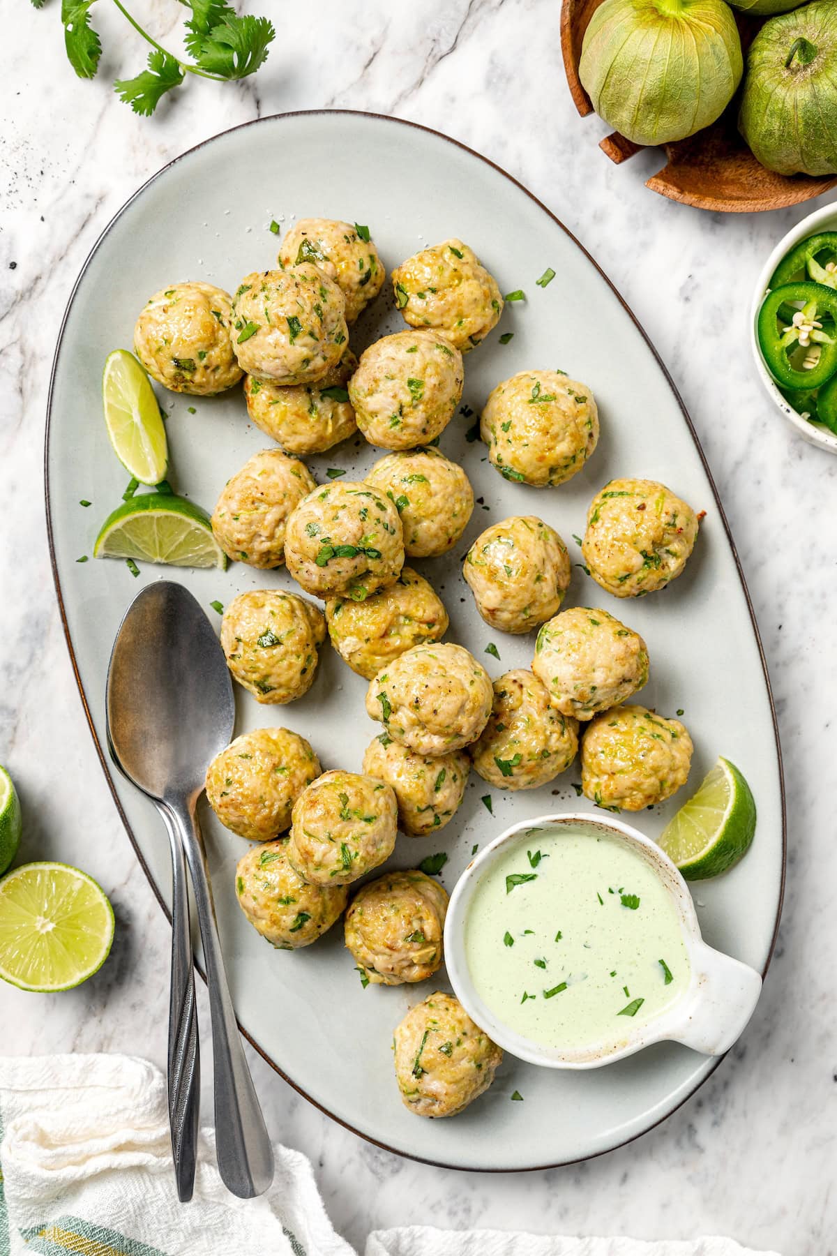 Baked southwest turkey meatballs on platter with bowl of creamy cilantro sauce.
